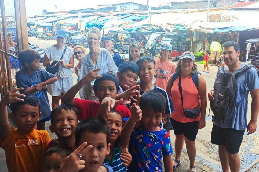 A group of people posing for a photo in an outdoor market with stalls and vehicles in the background. 4