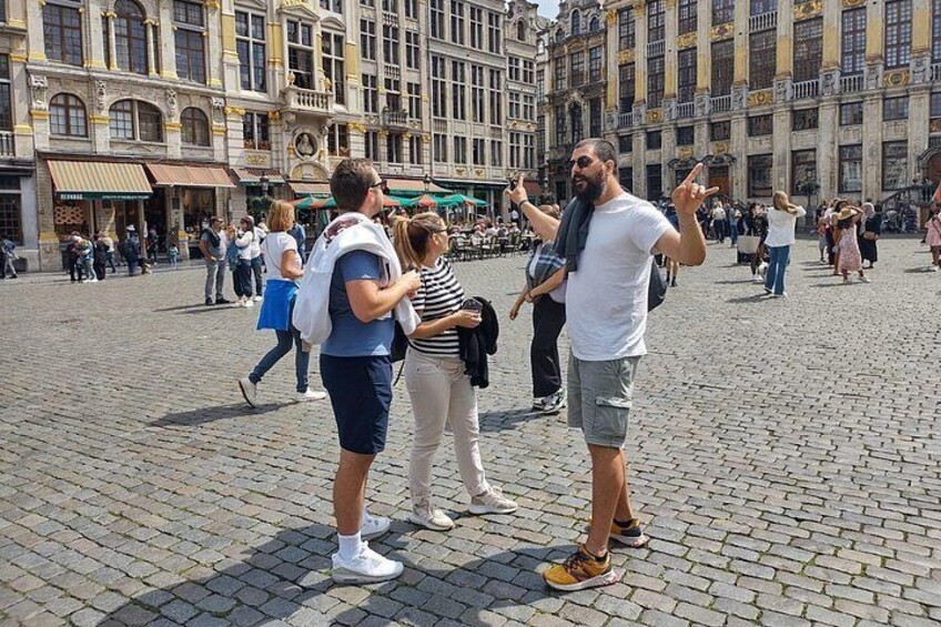 Una plaza empedrada con edificios históricos, turistas y un hombre gesticulando. 3