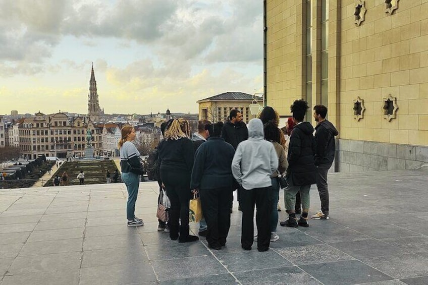 A group of people standing on a terrace overlooking a cityscape with a prominent tower and a building with star-shaped cutouts. 2