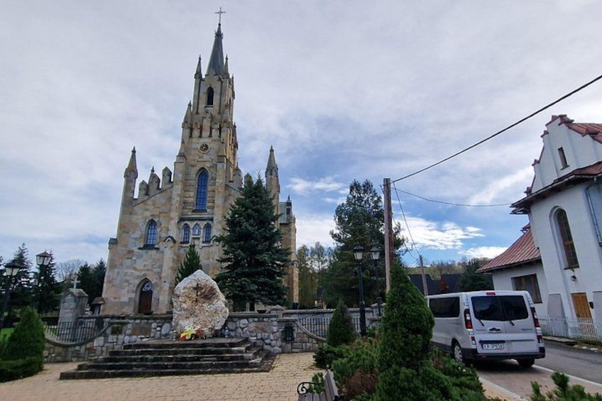 Una chiesa con un campanile slanciato, un monumento in pietra e un furgone bianco parcheggiato nelle vicinanze. 3