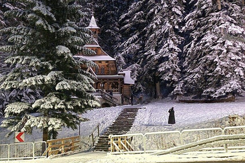 Un edificio imbiancato dalla neve con una scala che vi conduce, circondato da alberi carichi di neve. 1