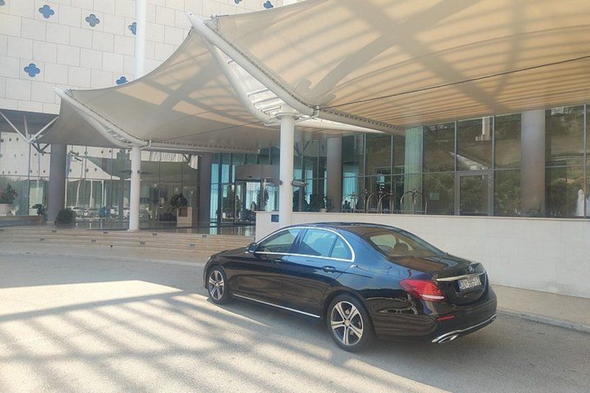 A black car parked in front of a modern building with a glass facade and a white canopy. 5
