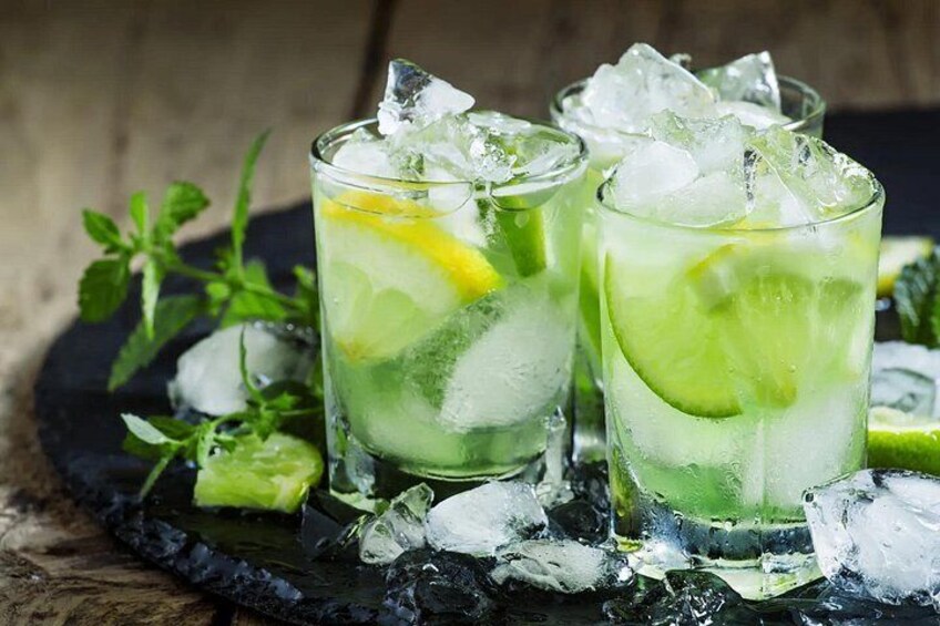 Two glasses of a lime-based beverage with ice cubes, garnished with lime slices, on a dark slate surface with mint leaves. 2