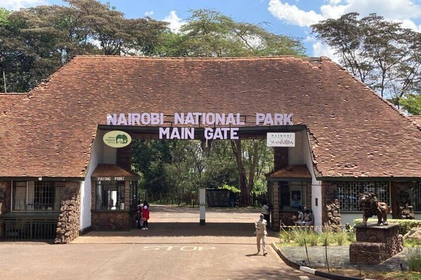 Haupttor des Nairobi Nationalparks mit einem Schild, einer Steinstruktur und einer Person, die davor steht. 2