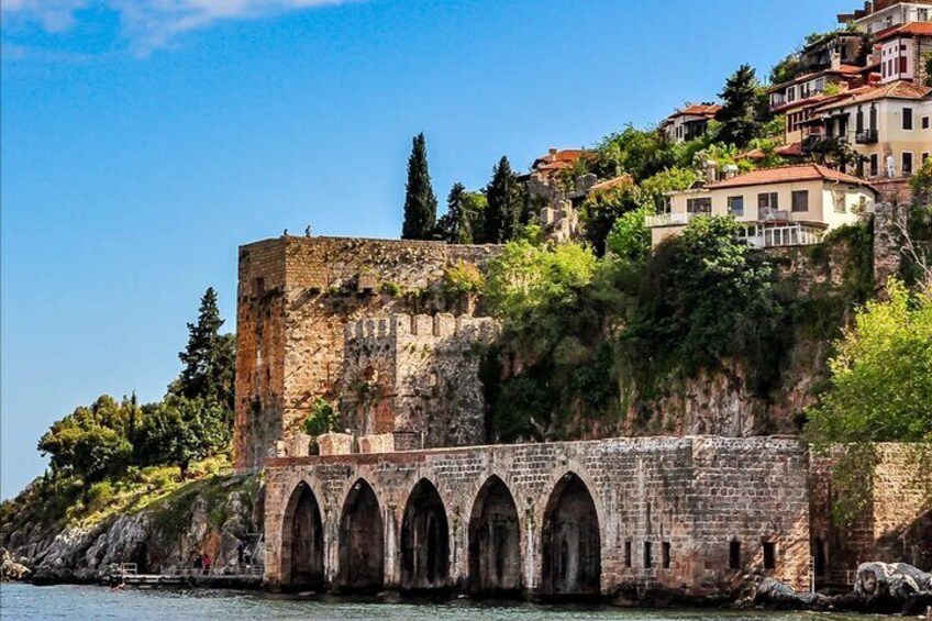 Eine historische Steinbrücke mit Bögen, eine Burg auf einem Hügel und Küstengebäude. 2