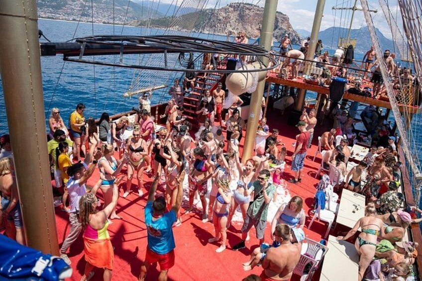 A crowded boat with people standing and sitting, a red deck, and a body of water with mountains in the background. 5