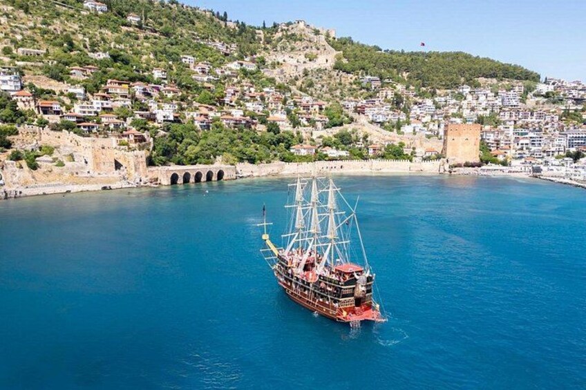 A sailing ship on a calm blue sea, a historic stone tower, and a densely built hillside town. 2