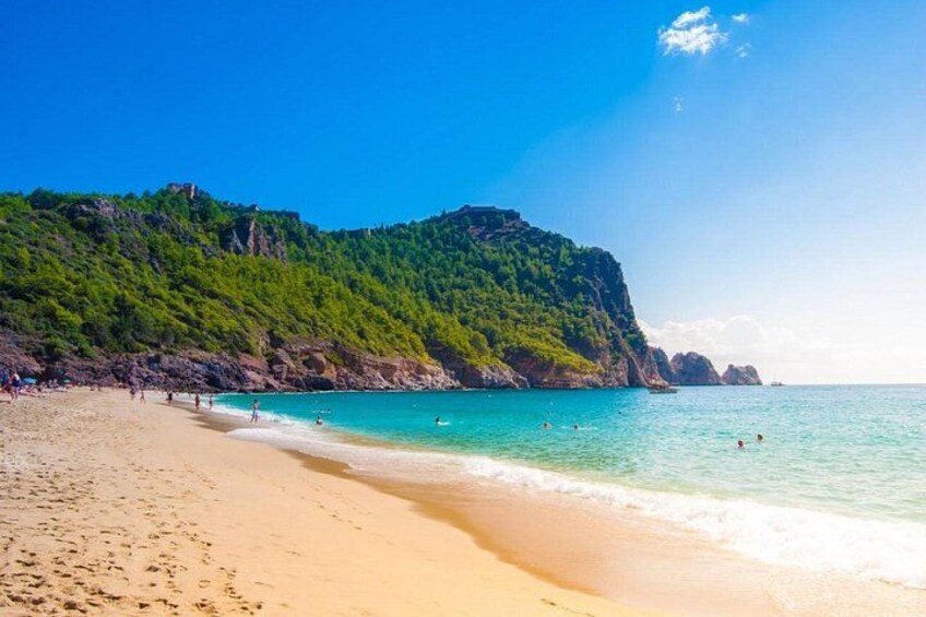 A beach with clear turquoise water, sandy shore, and a green hill in the background. 3