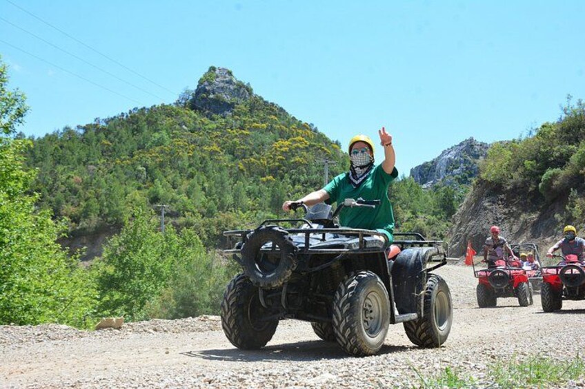 Una persona conduce un cuatrimoto por un camino de grava, con un paisaje montañoso al fondo. 1