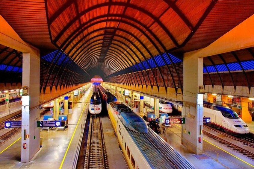 A modern train station with multiple tracks, trains, and overhead signage. 3