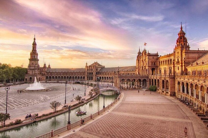 A grand plaza with a fountain, a large building with a tower, and a river. 1