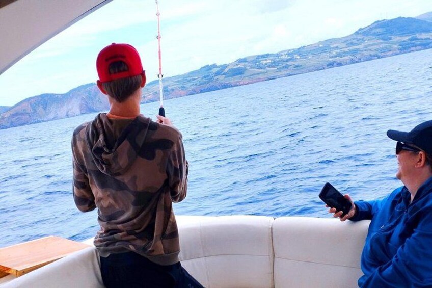 Dos personas en un bote, una sosteniendo una caña de pescar y la otra usando un teléfono inteligente. 3