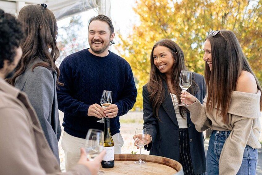 Un grupo de personas reunidas alrededor de una mesa con botellas de vino y copas. 3