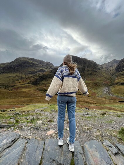 A person standing on a rocky outcrop overlooking a valley with mountains in the background. 1