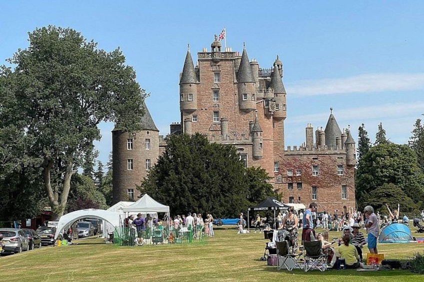 A castle with turrets and a grassy field with people and tents. 3