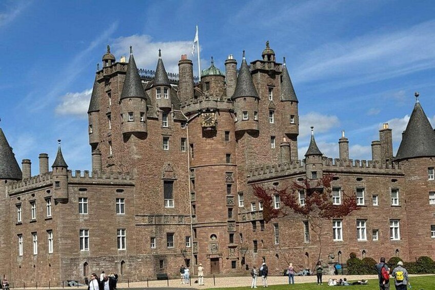 A large, historic castle with multiple towers and turrets, surrounded by a well-maintained lawn and a few people in the foreground. 4