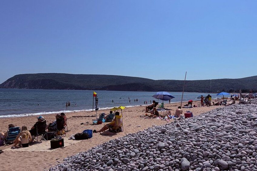 Una playa con gente tomando el sol, sombrillas y una costa rocosa. 5