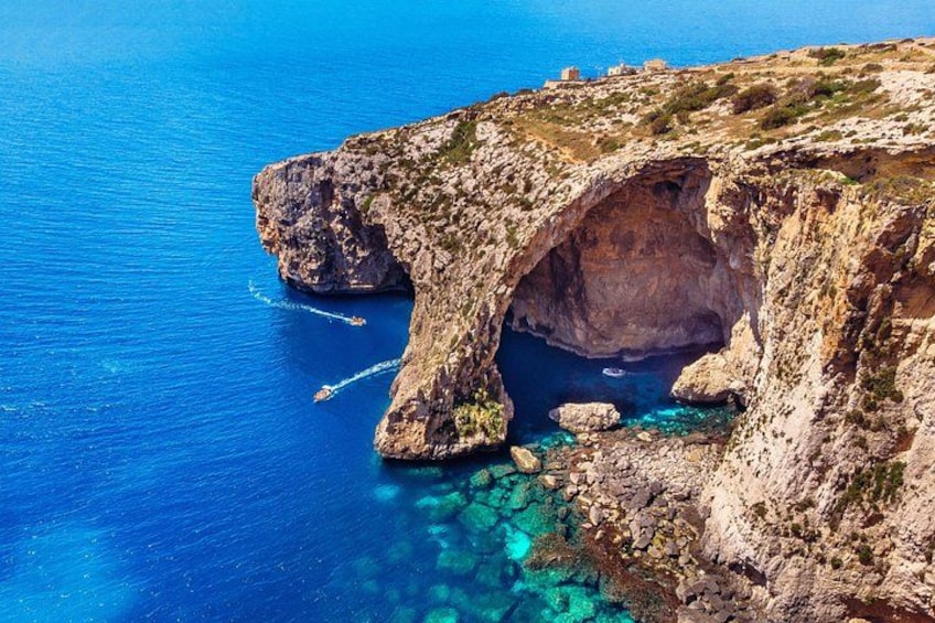 A coastal cliff with a natural arch formation, clear blue waters, and rocky terrain. 2