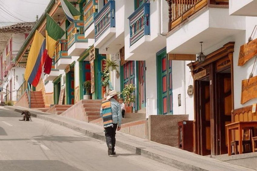 Una persona camina por una calle flanqueada por edificios coloridos, algunos con balcones y puertas. 3