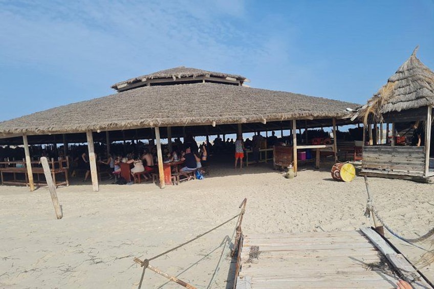 A beachside thatched-roof structure with people dining inside. 2