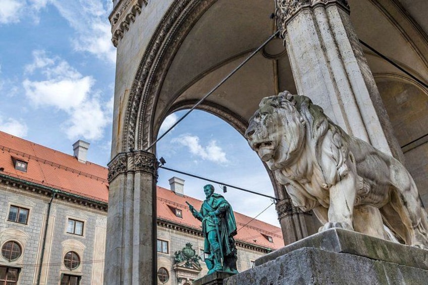 Eine Statue eines Mannes in grünen Roben unter einem Bogen, neben ihm eine Löwenstatue. 2
