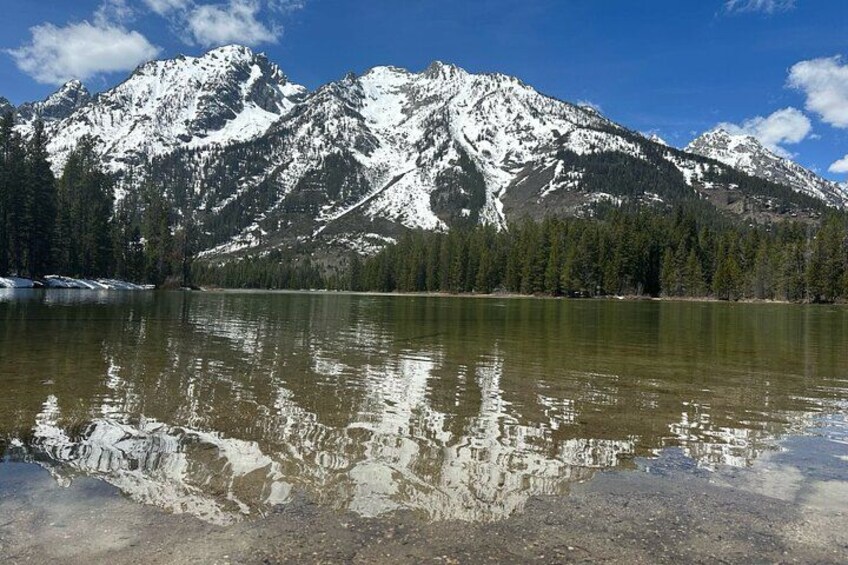 A mountain range with snow-capped peaks, a calm lake reflecting the mountains, and a clear blue sky. 2