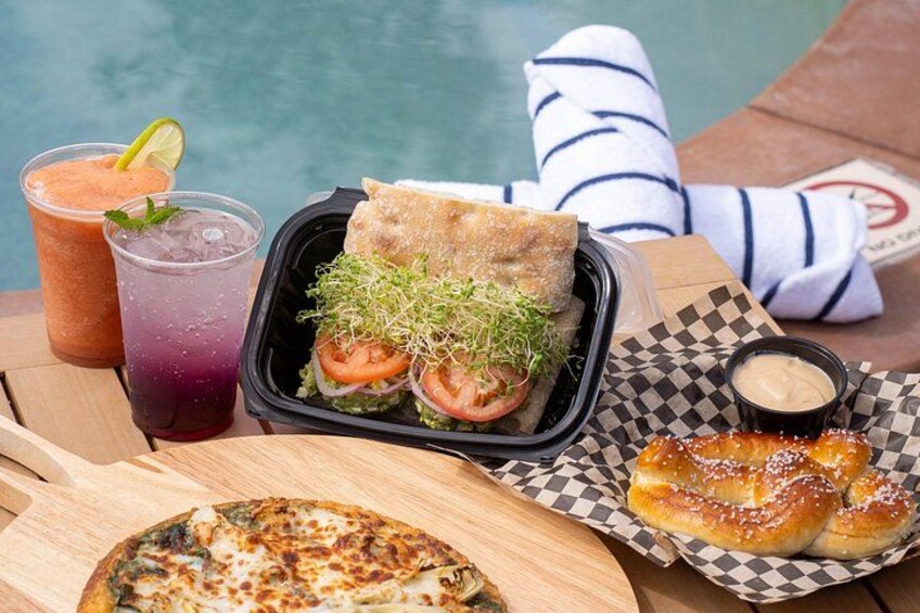 A meal by a poolside with a sandwich, a drink, and a pizza. 3