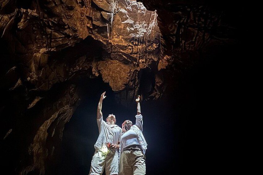 Two people in white robes reaching towards a rock formation in a cave. 1