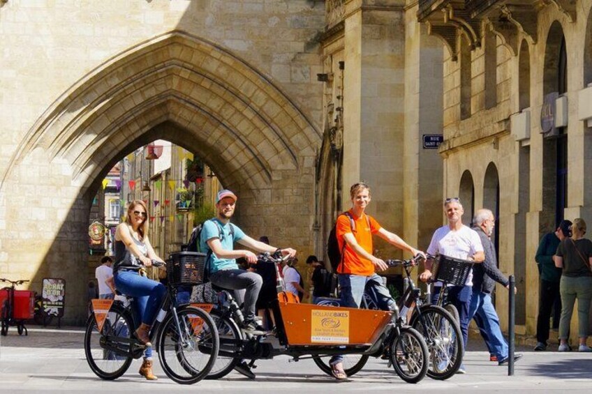 Eine Gruppe von Radfahrern, darunter auch ein Dreiradfahrer, bewegt sich in einer Stadt mit historischer Architektur. 2