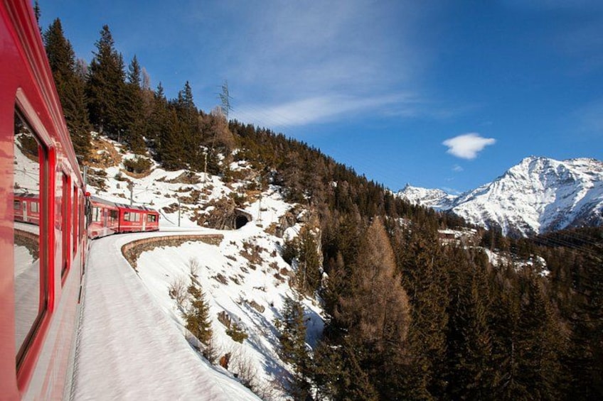 A red train on a snowy mountain track, surrounded by dense forests and snow-covered peaks. 3