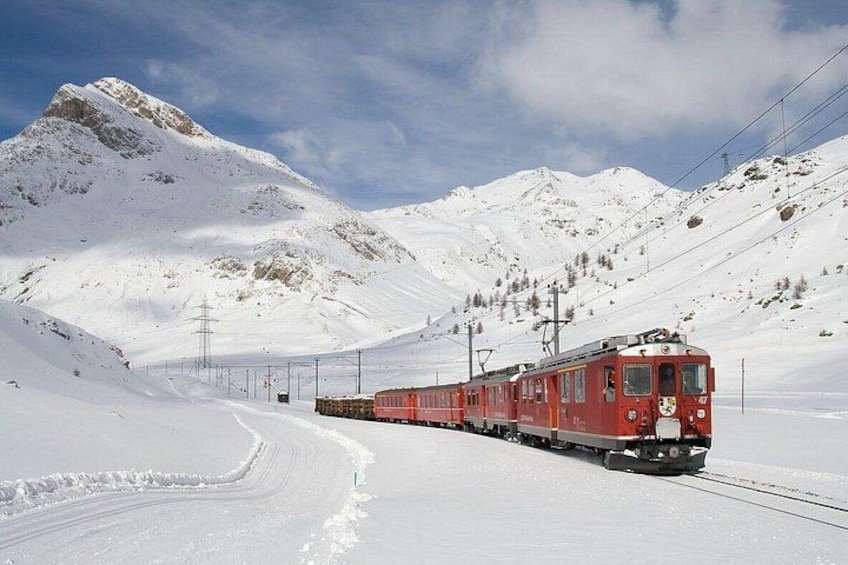 A red train on tracks in a snowy mountainous area. 2