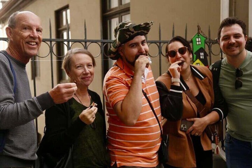 A group of people standing outdoors, some wearing casual clothing and one in a striped shirt. 5