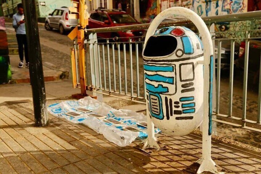 A white and blue robot figure standing on a sidewalk next to a metal fence. 3