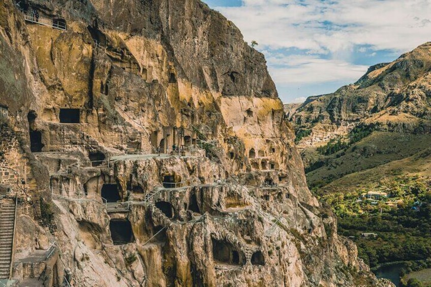 A cliffside with ancient rock-cut dwellings and a staircase. 3