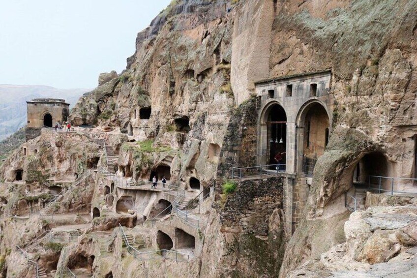 A rock-cut monastery with multiple cave dwellings and a staircase leading up the cliff. 5