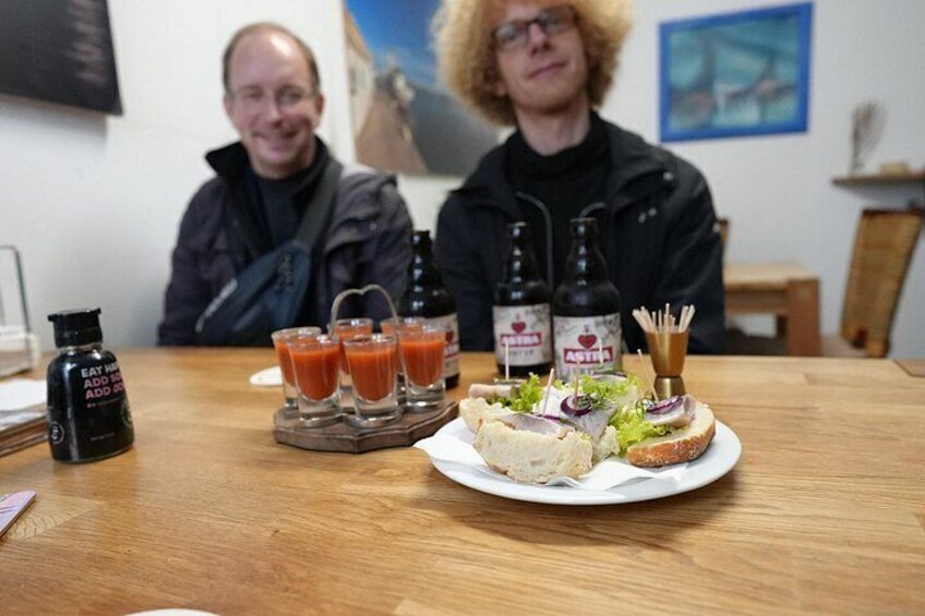A table with a plate of food, two bottles, and three glasses of a red beverage. 1