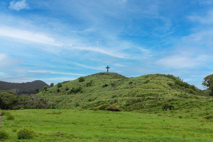 A grassy hill with a cross on top under a blue sky. 5