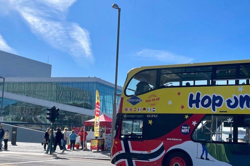 A double-decker bus with 'Hop On Hop Off' text, a modern building, and people walking. 5