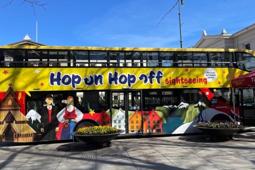 Un autobus a due piani con un murale colorato che pubblicizza un tour turistico Hop on Hop off. 1