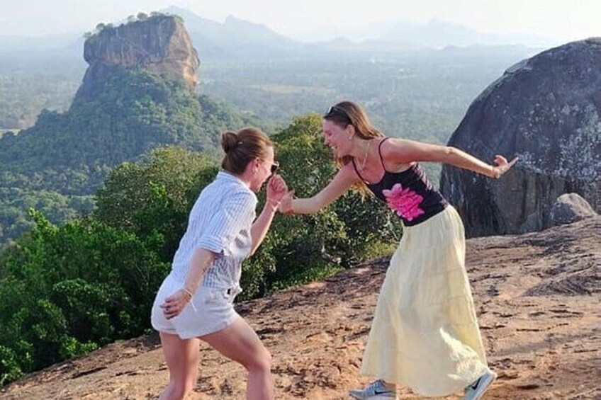 Two people dancing on a rocky outcrop with a mountainous landscape in the background. 3