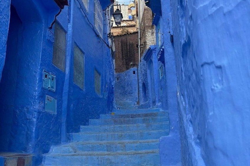 A narrow street flanked by buildings painted in blue, leading up a set of stairs. 5