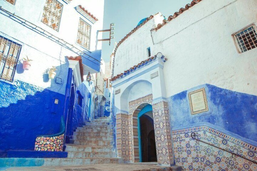 A narrow street with blue-painted buildings, a staircase, and an ornate doorway. 4