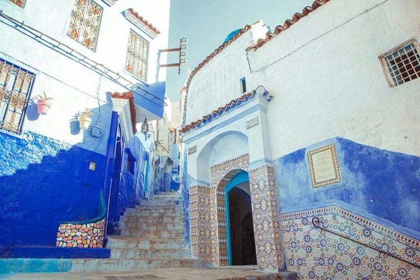 A narrow street with blue-painted buildings, a staircase, and a decorative archway. 3