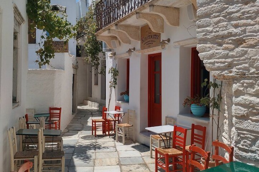 Une rue étroite bordée de bâtiments blancs, de portes rouges et de terrasses avec des chaises et des tables rouges. 4