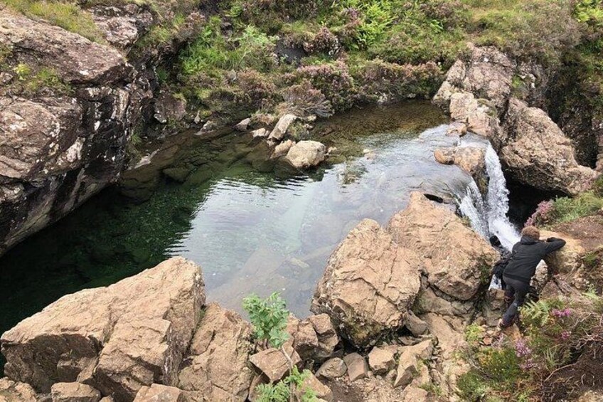 A rocky landscape with a small waterfall, clear water, and a person standing on the rocks. 4