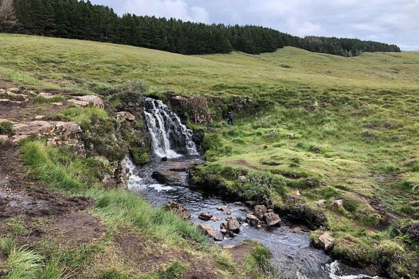 A waterfall in a grassy field with a person standing nearby. 5