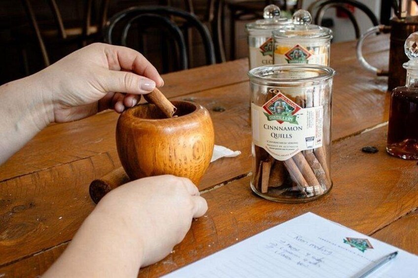 A wooden table with a hand stirring a spice container, a jar of cinnamon quills, and a notebook. 5