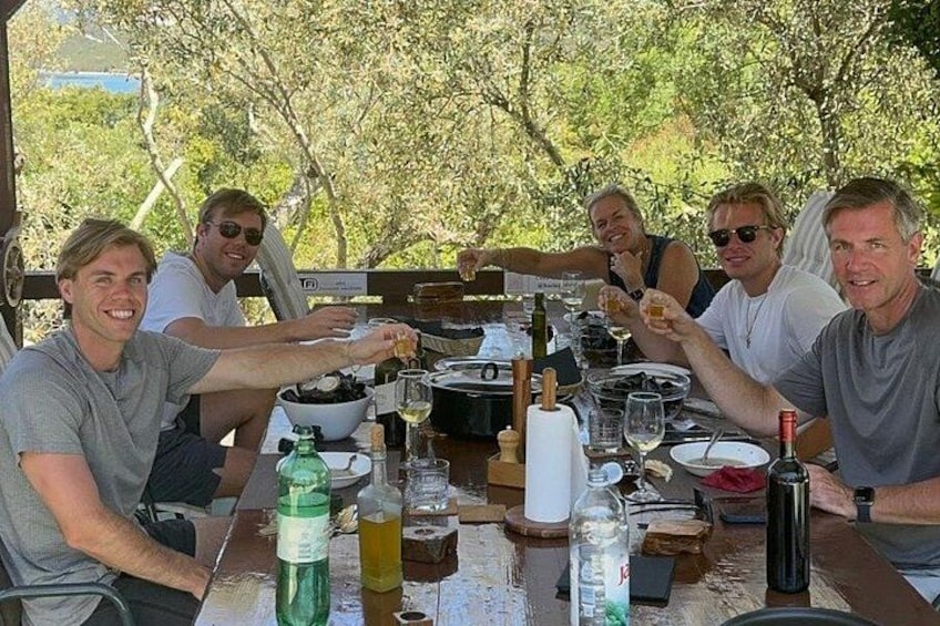 Een groep mensen die met drankjes en eten proost aan een tafel. 2