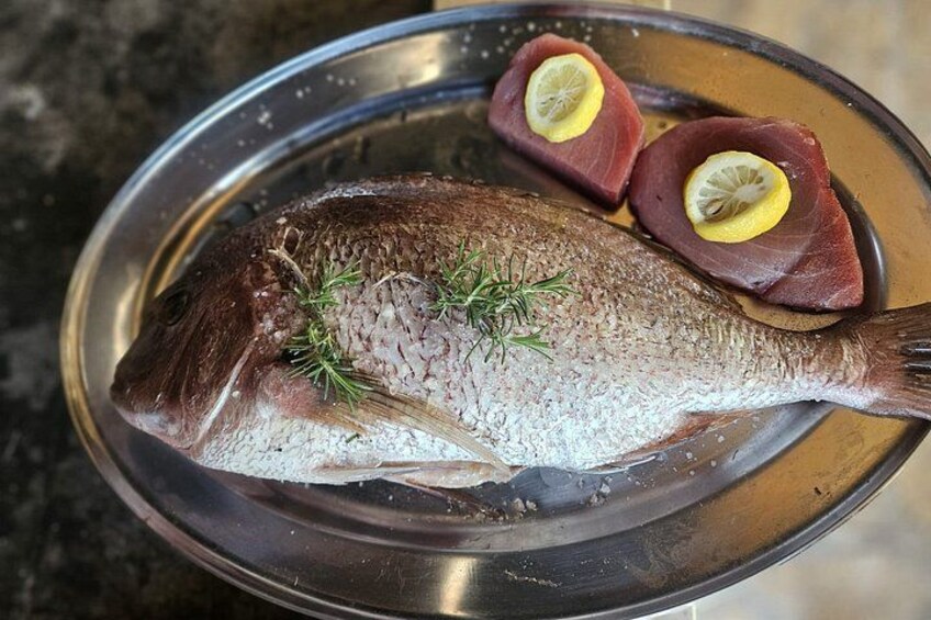 Un pescado entero con rodajas de limón y hierbas sobre un plato de metal. 5