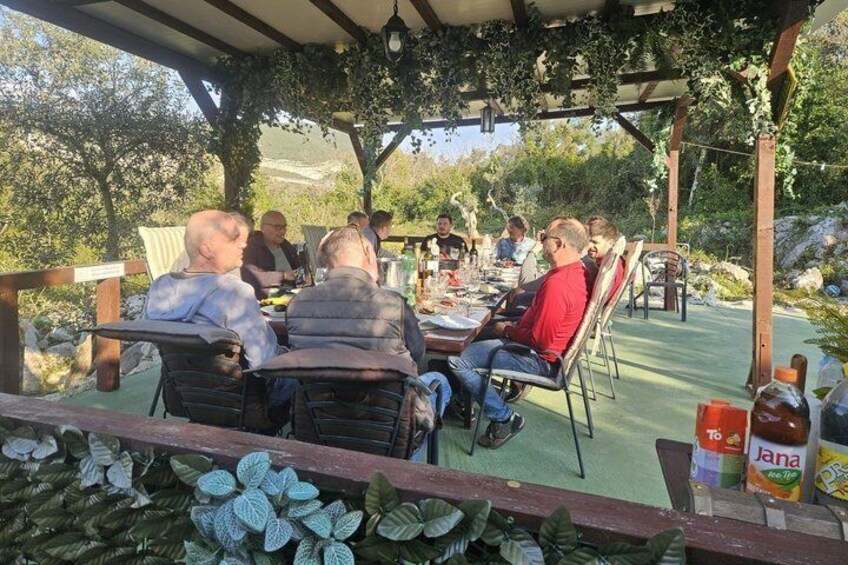 Un grupo de personas sentadas en una mesa al aire libre bajo una pérgola, rodeadas de vegetación. 4